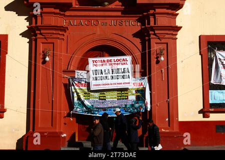 Die Menschen gehen an Schildern am Eingang des Palacio de Justicia/Justice Palace vorbei, die einen unbefristeten Streik der Arbeiter ankündigen, die das Gebäude übernommen haben. Plaza de Armas Central Square, Puno, Peru. Es ging um die Einbeziehung von Justizarbeitern in ein neues Gesetz für Beamte (das ihrer Meinung nach die Autonomie des Rechtssystems bedroht) und um Änderungen des Gehaltssystems. Stockfoto