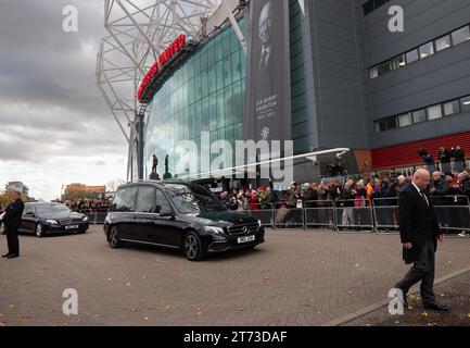 Manchester, Großbritannien. 13. November 2023. Sir Bobby Charlton's Leichenwagen passiert den Old Trafford Football Ground, wo Blumen und Nachrichten an der Gedenkstätte für die Münchner Katastrophe von 1958 hinterlassen wurden. Der Leichenwagen ging an der Trinity Statue vorbei und ging über den Sir Matt Busby Way zum Begräbnis im Stadtzentrum von Manchester. Bild: Garyroberts/worldwidefeatures.com Credit: GaryRobertsphotography/Alamy Live News Stockfoto