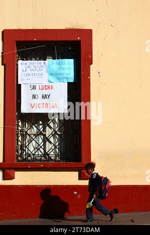 Ein Schuljunge geht an Schildern an einem Fenster des Palacio de Justicia/Justice Palace vorbei, die einen unbefristeten Streik von Arbeitern ankündigen, die das Gebäude übernommen haben. Plaza de Armas Central Square, Puno, Peru. Es ging um die Einbeziehung von Justizarbeitern in ein neues Gesetz für Beamte (das ihrer Meinung nach die Autonomie des Rechtssystems bedroht) und um Änderungen des Gehaltssystems. Stockfoto