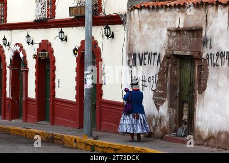 Eine Aymara-Frau in traditioneller Kleidung geht an einem alten Haus vorbei, das auf dem Plaza de Armas Central Square in Puno, Peru, verkauft wird Stockfoto