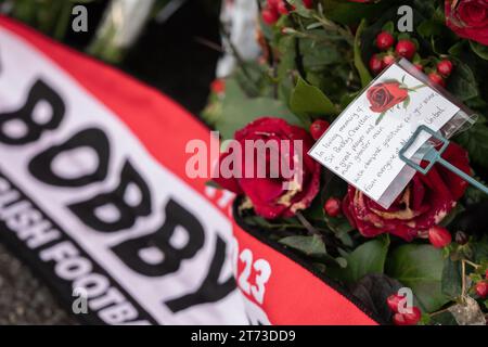 Manchester, Großbritannien. 13. November 2023. Sir Bobby Charlton's Leichenwagen passiert den Old Trafford Football Ground, wo Blumen und Nachrichten an der Gedenkstätte für die Münchner Katastrophe von 1958 hinterlassen wurden. Der Leichenwagen ging an der Trinity Statue vorbei und ging über den Sir Matt Busby Way zum Begräbnis im Stadtzentrum von Manchester. Bild: Garyroberts/worldwidefeatures.com Credit: GaryRobertsphotography/Alamy Live News Stockfoto