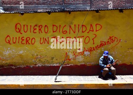 Quiero dignidad Quiero un trabajo / Ich will würde, Graffiti an der gelben Wand und Mann, der mit einer kleinen Gitarre in der Straße, Puno, Peru, Busking macht Stockfoto