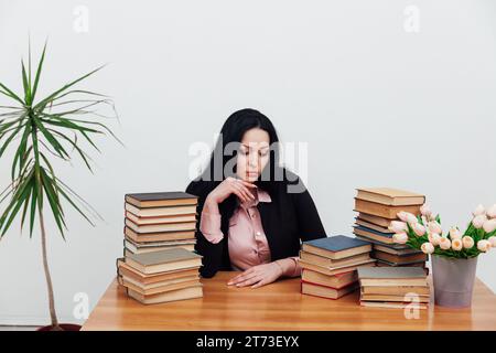 Eine Frau in der Bibliothek sitzt an einem Tisch mit einem Stapel Bücher Stockfoto