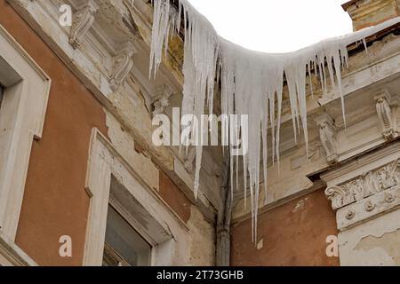 Riesige Eiszapfen hängen an der Traufe eines alten Gebäudes und drohen zu fallen. Stockfoto