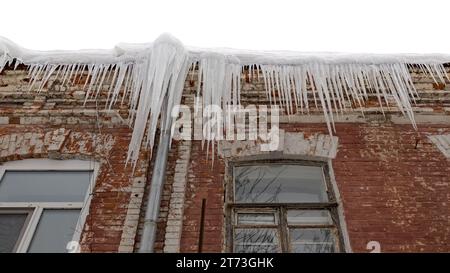 Riesige Eiszapfen hängen an der Traufe eines alten Gebäudes und drohen zu fallen. Stockfoto