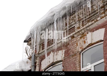 Riesige Eiszapfen hängen an der Traufe eines alten Gebäudes und drohen zu fallen. Stockfoto