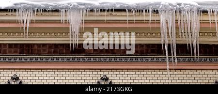 Riesige Eiszapfen auf der Traufe eines alten Gebäudes. Stockfoto
