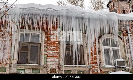 Riesige scharfe Eiszapfen hängen gefährlich vom Dach eines alten Hauses. Stockfoto