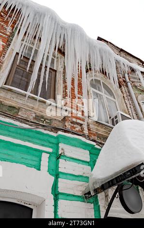 Riesige scharfe Eiszapfen hängen gefährlich vom Dach eines alten Hauses. Stockfoto