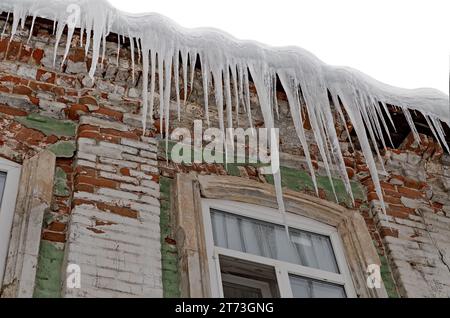 Riesige scharfe Eiszapfen hängen gefährlich vom Dach eines alten Hauses. Stockfoto