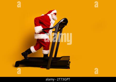 Profilseitenfoto des coolen verrückten pensionierten Mannes santa claus Training Laufband leerer Raum isoliert auf gelbem Hintergrund Stockfoto