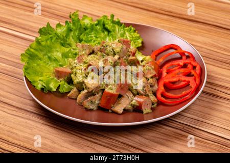 Salat mit Wurstscheiben in weißer Soße mit Paprikaringen auf einem Teller auf einem Holztisch Stockfoto