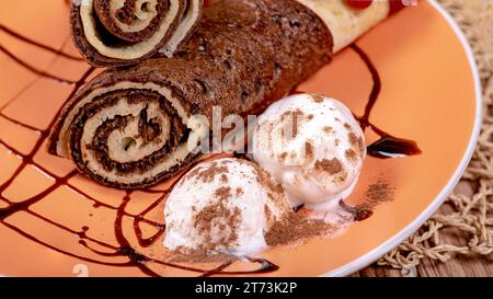 Schokoladenrollen und Eiskugeln, bestreut mit Schokoladenchips auf einem Teller Stockfoto