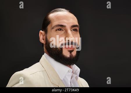 Porträt eines fröhlichen bärtigen arabischen Mannes in weißem Hemd und elegantem Blazer, der auf schwarzem Hintergrund posiert Stockfoto