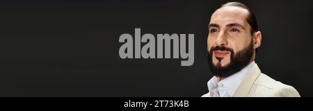 Porträt eines fröhlichen bärtigen arabischen Mannes in weißem Hemd und Blazer, der auf schwarzem Hintergrund posiert, Banner Stockfoto