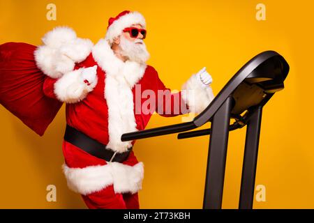 Foto von fröhlicher lustiger Rentner santa claus Charakter, der Geschenke liefert, die auf gelbem Hintergrund isoliert aussahen Stockfoto