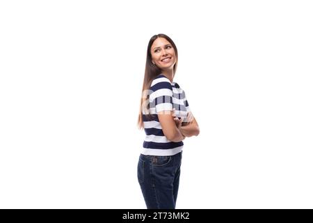 Attraktive junge brünette Frau in einem gestreiften T-Shirt steht im Profil auf weißem Hintergrund mit Kopierraum Stockfoto