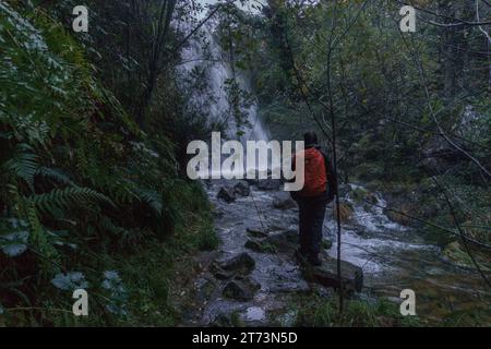 Wanderer steht am Wasserfall Cascata de Leonte an einem dunklen Herbstabend im Nationalpark Geres, Vilar da Veiga, Portugal Stockfoto