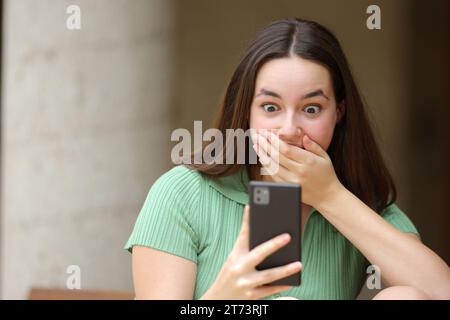 Vorderansicht Porträt einer überraschten Frau, die auf der Straße Nachrichten über Mobiltelefone überprüft Stockfoto