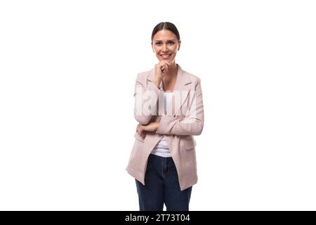 Eine angenehme junge Frau mit schwarzen Haaren in einer Jacke steht nachdenklich auf einem weißen Hintergrund mit Kopierraum Stockfoto