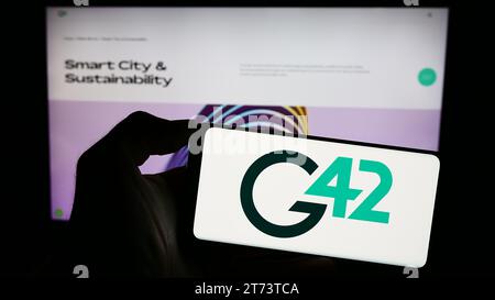 Person, die ein Mobiltelefon mit dem Logo des Emirati Technology Company Group 42 Holding Ltd. Hält (G42) vor der Webseite. Schwerpunkt auf dem Display des Telefons. Stockfoto