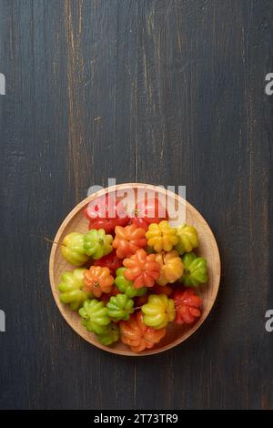 surinam-Kirschen, eugenia uniflora, alias pitanga, brasilianische oder Cayennekirsche, lebendige bunte Früchte auf Holzteller, isoliert auf schwarzem rustikalem Backgr Stockfoto