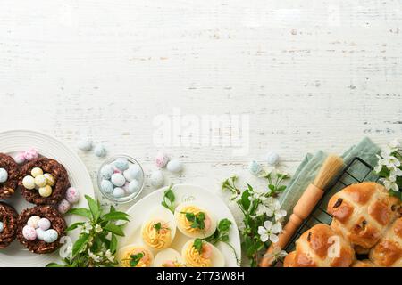 Osterbrunch oder Osterfrühstück. Osterschokolade-Nest-Kuchen mit Schokoladeneiern, traditionellen heißen Kreuzbrötchen und teuflischen Eiern mit Blumensträußen Stockfoto