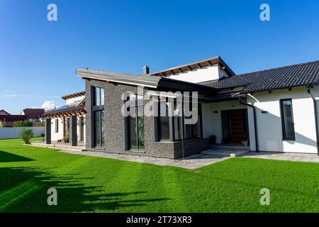 Modernes Haus mit grauer Steinmauer und weißen Wänden in einem Garten mit frischem grünem Gras Stockfoto