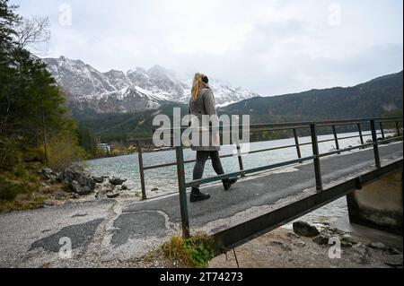 Wetter in Bayern, eine Frau läuft über eine Brücke am Eibsee. Im Hintergrund ist die durch Nebel verhüllte Zugspitze zu sehen. Bei milden Temperaturen und leicht bedecktem Himmel, lädt die bezaubernde Landschaft zu einem Ausflug in die Natur ein. Grainau Bayern Deutschland Grainau *** Wetter in Bayern, Eine Frau geht über eine Brücke am Eibsee im Hintergrund sieht man die in Nebel gehüllte Zugspitze bei milden Temperaturen und einen leicht bewölkten Himmel, die zauberhafte Landschaft lädt zu einem Ausflug in die Natur Grainau Bayern Deutschland Grainau ein Copyright: x xonw-imagesx/xMariusxBullingx Stockfoto