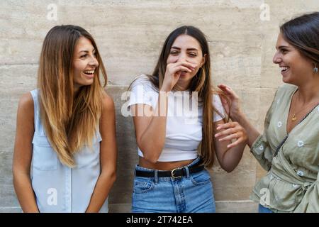 Drei junge Frauen teilen sich einen unbeschwerten Moment, lachen und genießen die Gesellschaft der anderen in einer offenen Umgebung. Stockfoto