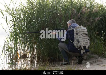 Mann mit Jagdgewehr in der Nähe des Sees im Freien. Leerzeichen für Text Stockfoto