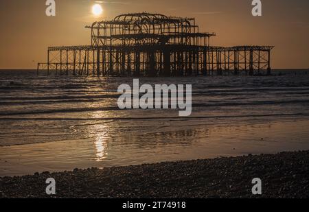 Sonnenuntergang hinter den Ruinen des alten Westpiers an der Küste in Brighton, Sussex, England, Großbritannien Stockfoto