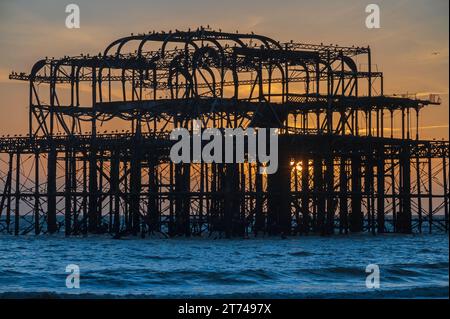 Sonnenuntergang hinter den Ruinen des alten Westpiers an der Küste in Brighton, Sussex, England, Großbritannien Stockfoto