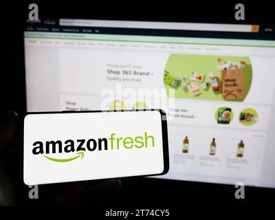 Person mit Smartphone und Logo des US-amerikanischen Lebensmitteleinzelhandelsunternehmens Amazon Fresh vor der Website. Schwerpunkt auf dem Display des Telefons. Stockfoto