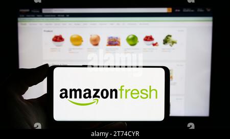 Person, die ein Mobiltelefon mit dem Logo des US-amerikanischen Lebensmitteleinzelhandelsunternehmens Amazon Fresh vor der Webseite hält. Schwerpunkt auf dem Display des Telefons. Stockfoto