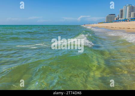 Blick auf die Küste mit architektonischen Gebäuden unter blauem Himmel am Horizont, begleitet von sanften Wellen, die auf den Sandstrand Rollen. Miami Beach, Florida, Stockfoto