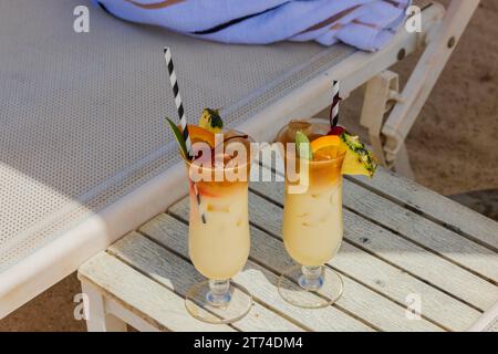 Nahaufnahme von zwei Cocktailgläsern auf weißem Tisch am Sandstrand unter der Sonnenliege in Curacao. Stockfoto