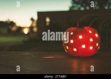 Eine beleuchtete Jack o' Laterne, die an einem Herbstabend in der Nähe der Dunkelheit auf einer Veranda sitzt, mit verschwommenem Hintergrund und einer Vintage-Ästhetik. Stockfoto
