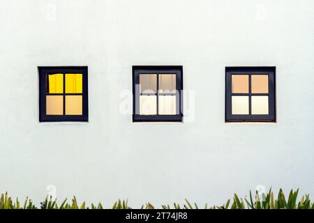 Vier Fenster in zwei verschiedenen Stilen, die an der Seite eines weißen Ziegelgebäudes vor einem klaren blauen Himmel montiert sind Stockfoto