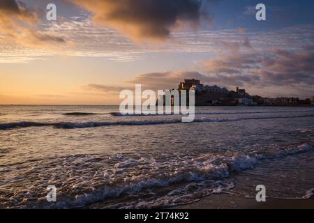 Wunderschöne Landschaft der Altstadt von Peniscola mit dem Schloss auf der Spitze und den Meereswellen am Strand im Vordergrund bei Sonnenaufgang, Peníscola, CA Stockfoto