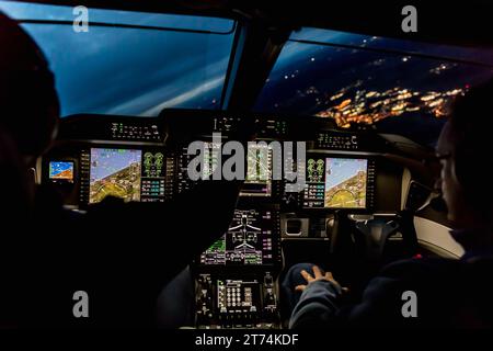 Blick aus dem Cockpit eines modernen Flugzeugs, das bei Nacht in einer beleuchteten Vilage landet. Beleuchtetes Cockpit-Armaturenbrett aus Glas bei der Landung am Flughafen Stockfoto