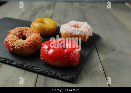 Vier bunte glasierte Donuts auf einem schwarzen, grauen Hintergrund. Stockfoto