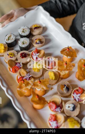 Der nicht erkennbare Kellner hält ein großes weißes Gericht mit verschiedenen leichten Snacks und Sushi in den Händen. Stockfoto