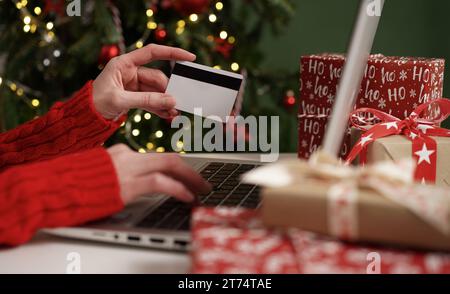 Junge Frau mit Kreditkarte und macht Einkäufe auf einem Laptop vor dem Hintergrund der Weihnachtsdekoration und Geschenke, Nahaufnahme. Weihnachten und Neues Jahr Stockfoto