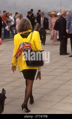 1990er Jahre Mode UK stilvolle englische Frau in leuchtend gelber Jacke und schwarzem modischem Rock, schwarzen Strumpfhosen und schwarzen Schuhen. Zwei Union Jack Flaggen sind in ihrer schwarzen Handtasche. Derby Day Pferderennen Epsom Downs, Surrey, England, Juni 1990 1990er, UK HOMER SYKES Stockfoto
