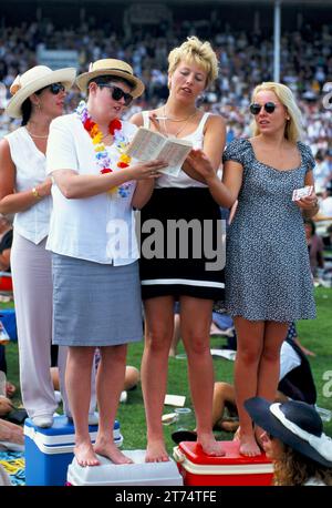 Gruppe junger Frauen, die auf Picknickboxen stehen, um einen besseren Blick auf das Pferderennen zu erhalten. Sie studieren die Rennkarte und hoffen auf das Beste. Royal Ascot Pferderennen. Ascot, Berkshire, England, ca. 2005 2000. Juni, UK HOMER SYKES Stockfoto