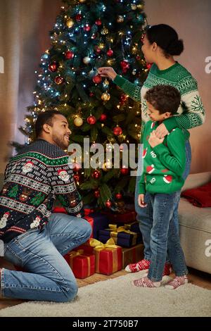 Vertikale Aufnahme der modernen afroamerikanischen Familie neben dem Weihnachtsbaum, der sich anlächelt Stockfoto