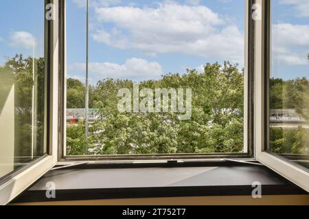 Ein Blick von außen aus einem Fenster mit weißen Wolken am Himmel und grünen Bäumen auf der anderen Seite des Fensters Stockfoto