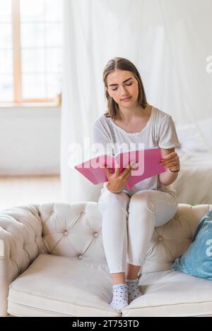 Portrait der jungen Frau, die Buch nach Hause liest Stockfoto