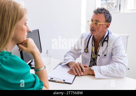 Männlicher Arzt, der seinem Patienten ihre Diagnose in seiner Arztpraxis erzählt Stockfoto